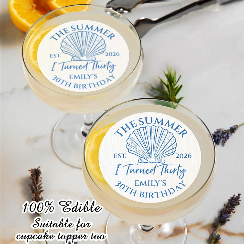 以下が含まれることがあります： レモンスライスと白い食べられるトッピングが付いた、2つの透明なカクテルグラス。トッピングには青い貝殻のデザインと「The Summer, I Turned Thirty, Emily's 30th Birthday」という文字が書かれています。「100% Edible」という文字も表示されています。