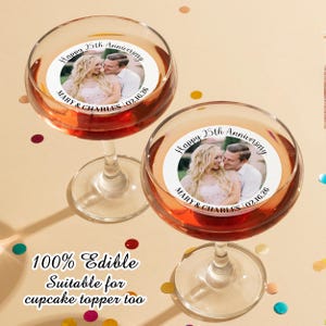 May include: Two clear glass champagne flutes with edible cupcake toppers. The toppers are round and feature a photo of a couple with the text "Happy 25th Anniversary Mary & Charles 02.16.26".