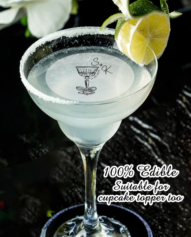 May include: A clear glass margarita glass with a white, round, edible topper that says "S+K 11.20.2020". The topper is decorated with a drawing of a martini glass with a bow. A lime wedge is on the rim of the glass. The text "100% Edible Suitable for cupcake topper too" is below the glass.