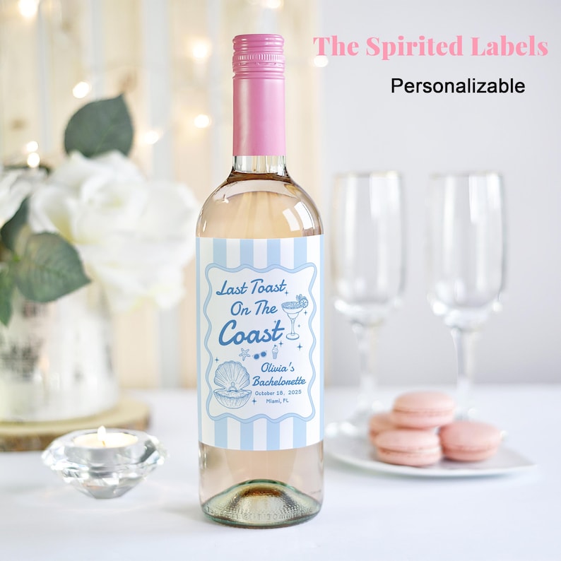 May include: A personalized wine bottle label with a blue and white striped background. The label features a seashell, a cocktail glass, and the text "Last Toast, On The Coast Olivia's Bachelorette October 18, 2023 Miami, FL".