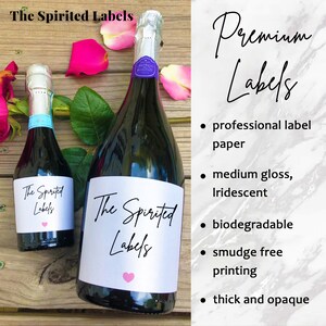 May include: Two bottles of sparkling wine with labels that say "The Spirited Labels". The labels are white with black text and a pink heart. The bottles are on a wooden surface with rose petals.