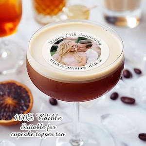 May include: A white round edible cake topper with a photo of a couple and the text "Happy 25th Anniversary Mary & Charles 02.16.26". The topper is on top of a brown drink in a martini glass. The text "100% Edible Suitable for cupcake topper too" is below the glass.