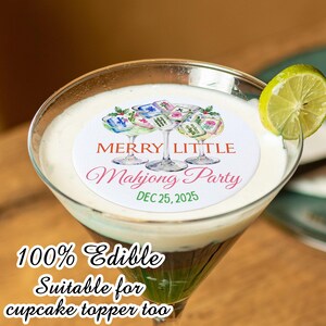 May include: A cocktail in a martini glass with a lime wedge. The drink has a white foamy top and a green base. A white circular edible cupcake topper features the text "Merry Little Mahjong Party" and "Dec 25, 2025".