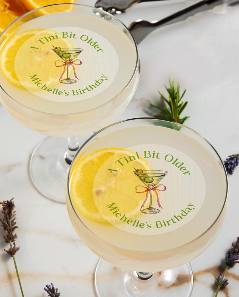 May include: Two martini glasses with a lemon slice and a sticker that says "A Tini Bit Older Michelle's Birthday" with a drawing of a martini glass with olives.