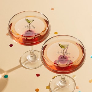 May include: Two martini glasses filled with a pink beverage. Each glass has a round sticker with a martini glass illustration and the text "Michelle's Birthday A TINI BIT OLDER".