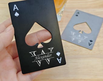 May include: Black metal bottle opener shaped like an ace of spades playing card with a cut-out spade for opening bottles. The card has the letter "A" and a spade symbol in the top left corner. The card also has the name "Alexander" and a spade symbol in the bottom right corner.