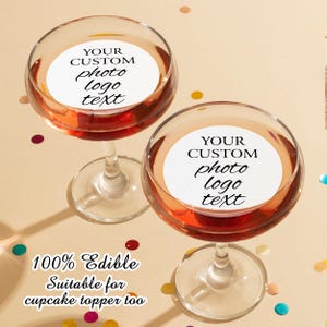 May include: Two clear glass champagne flutes with edible cupcake toppers. The toppers are white circles with black text that reads "YOUR CUSTOM photo logo text". The text is 100% edible and suitable for cupcake toppers.