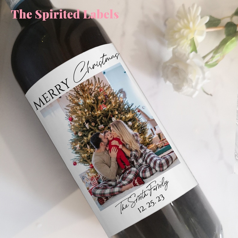 May include: A dark wine bottle with a custom label. The label reads "MERRY Christmas" in script above a family photo in front of a Christmas tree. The family name and date are below the photo. The Spirited Labels logo is at the top.
