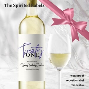 May include: A white wine bottle with a label that says "Twenty ONE" in purple and black script. The label also says "Finally Legal Happy Birthday Carolina September 16, 2021".