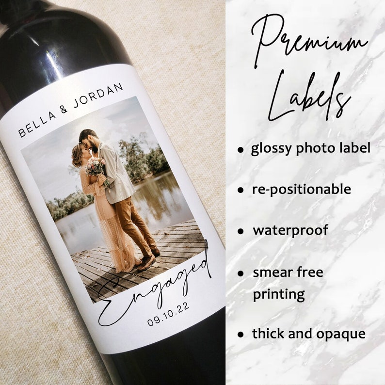 May include: A wine bottle with a custom label featuring a photo of a couple, the names "BELLA & JORDAN", and the word "Engaged" with the date "09.10.22". The label also lists features like "glossy photo label" and "waterproof".