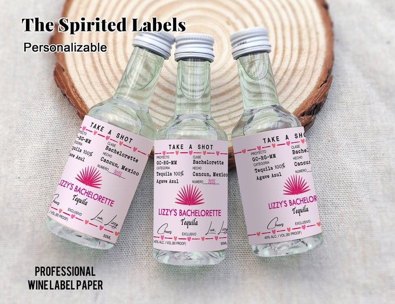 May include: Three small clear glass bottles with pink and white labels. The labels feature a pink sunburst design and the text "Lizzy's Bachelorette Tequila" and "Lizzy's Bachelor Tequila".