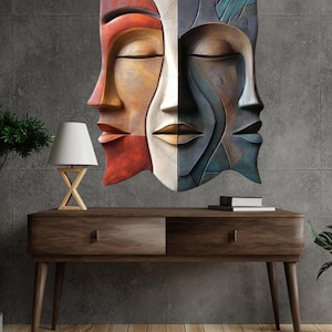 May include: A multi-colored wall sculpture depicting three stylized faces with closed eyes. The sculpture is mounted on a gray wall above a wooden console table. The faces are in shades of red, orange, white, and blue.
