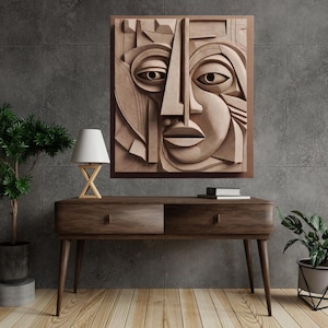 May include: A large, square, abstract relief sculpture of a face with geometric features. The artwork is in shades of brown and tan, mounted in a dark brown frame. The sculpture hangs above a wooden console table with a lamp and plants.