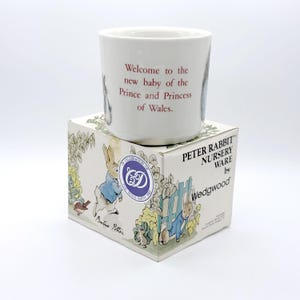 May include: A white ceramic Peter Rabbit nursery ware cup with the text "Welcome to the new baby of the Prince and Princess of Wales." The cup sits on a matching box with Peter Rabbit illustrations.