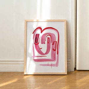 May include: A framed abstract painting with pink and red brushstrokes in the shape of a face. The background is white.