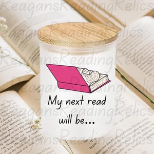 May include: White candle jar with a wooden lid. The jar has a pink and white illustration of a book with a heart inside. The text on the jar reads "My next read will be..."