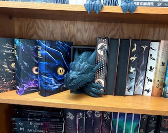 May include: A bookshelf with a variety of books, including a dragon figurine, and a book with the title "Fourth Wing" by Rebecca Yarros.