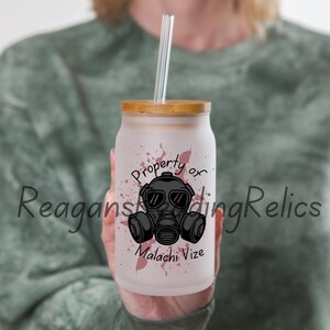Puede incluir: Un tarro de vidrio esmerilado con tapa de bambú y un gráfico de máscara de gas en blanco y negro. El tarro tiene salpicaduras de pintura rosa y el texto "Property of Malachi Vize".