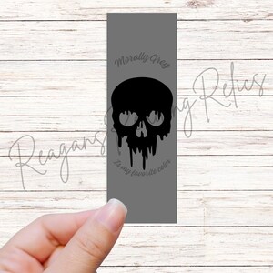 May include: A gray bookmark with a black skull design. The skull has a dripping effect, and the text "Morally Grey is my favorite color" is written on the bookmark.