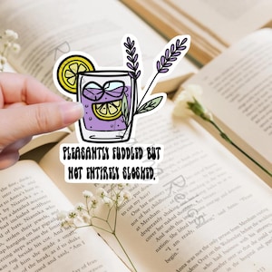 May include: A sticker with a purple drink with a lemon wedge and lavender sprigs. The text reads "Pleasantly Fuddled But Not Entirely Sloshed."
