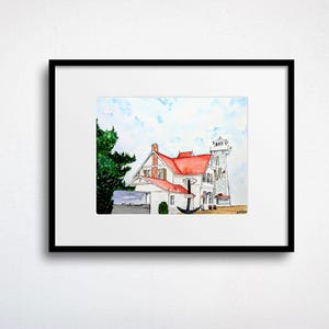May include: Watercolor painting of a white house with a red roof and a lighthouse. An anchor is in front of the house. The painting is framed in a black frame and set against a white background.