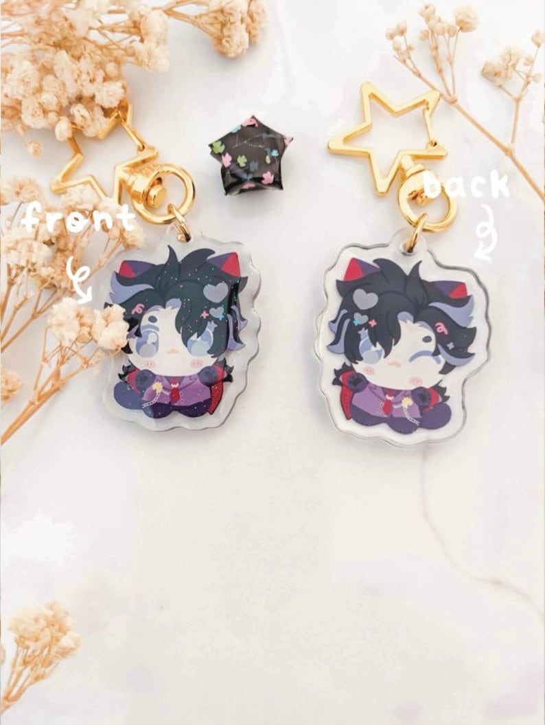 K&ouml;nnte beinhalten: Zwei Schl&uuml;sselanh&auml;nger im Anime-Stil mit goldenen sternf&ouml;rmigen Verschl&uuml;ssen. Jeder Schl&uuml;sselanh&auml;nger zeigt eine Cartoon-Figur mit schwarzen Haaren, roten Akzenten und einem lila Outfit. Ein kleiner, sternf&ouml;rmiger Anh&auml;nger mit schwarzem Blumenmuster ist ebenfalls vorhanden.