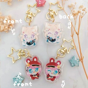 K&ouml;nnte beinhalten: Transparente Acryl-Schl&uuml;sselanh&auml;nger mit Anime-Charakteren und goldenen sternf&ouml;rmigen Verschl&uuml;ssen. Ein Design hat einen Charakter mit hellem Haar und einem schwarz-blauen Outfit. Das andere Design hat einen Charakter mit rosa Haaren und einem roten Outfit.