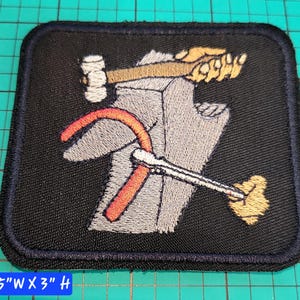 May include: Embroidered patch featuring a hammer, wrench, and sickle design on a black background. The patch is square with rounded corners and a navy blue border. The patch measures 3.5" wide by 3" high.