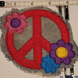 May include: Embroidered patch featuring a red peace sign with three colorful flowers. The flowers are pink, purple, and blue with yellow centers. The patch is on a denim background with frayed edges. The patch measures approximately 3 inches in width.