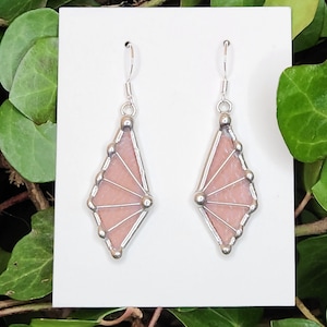 May include: A pair of pink and silver earrings. Each earring features a fan-shaped design with a pink glass center and silver-colored metal accents. The earrings have a simple hook closure.