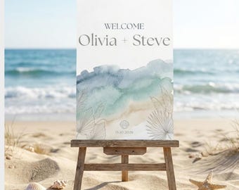 May include: A wooden easel displays a welcome sign on a sandy beach. The sign reads "WELCOME Olivia + Steve" above a watercolor design in blue, green, and beige. Seashells and a starfish are scattered on the sand.