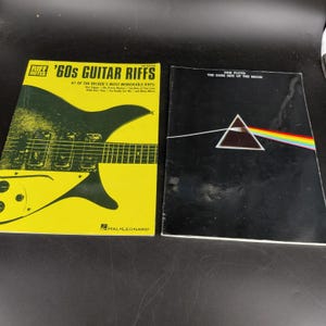 May include: Two music books: a yellow Riff Notes '60s Guitar Riffs book featuring a black electric guitar illustration, and a black Pink Floyd The Dark Side of the Moon songbook with the iconic white triangle and rainbow light prism graphic.