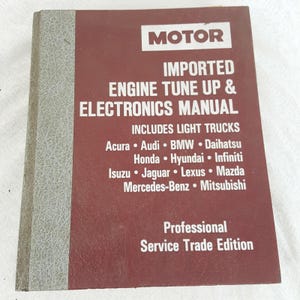 Peut inclure: Un manuel de réparation automobile Motor Imported Engine Tune Up & Electronics, de couleur marron et grise. La couverture indique "Includes Light Trucks" et énumère Acura, Audi, BMW, Daihatsu, Honda, Hyundai, Infiniti, Isuzu, Jaguar, Lexus, Mazda, Mercedes-Benz et Mitsubishi.