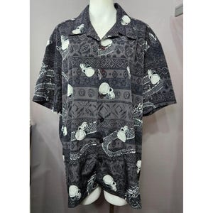 May include: A black and white short-sleeved button-up shirt with a skull and snake pattern. The shirt has a traditional Hawaiian shirt style.