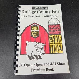以下が含まれることがあります： 赤い納屋の前に白い羊がいる。納屋には「2005 DuPage County Fair」と書かれている。羊は「Have "ewe" heard?」と書かれた吹き出しを持っており、「It's Fair Time!」という文字が羊の下にある。
