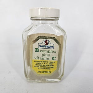 May include: A clear glass bottle with a white cap, labeled "SAFEWAY B complex plus vitamin C." The label includes text about the dietary supplement and the number of capsules. The bottle is rectangular with rounded edges.