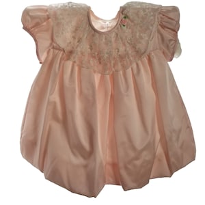 May include: A pale pink satin baby dress with a lace collar and a small pink flower embellishment.