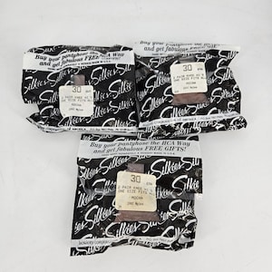 May include: Three sealed packages of "Silkies" brand knee-high pantyhose in Mocha. Each package has a label indicating size 30, "One Size Fits All," and 100% nylon. The packaging is black with white text and a repeating "Silkies" logo.
