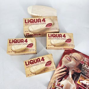 May include: An assortment of vintage LIQUA 4 Skin Cleansing System soap products. The image shows several boxes and a bar of soap, with the text "NEW" on the boxes. A magazine advertisement is also visible.
