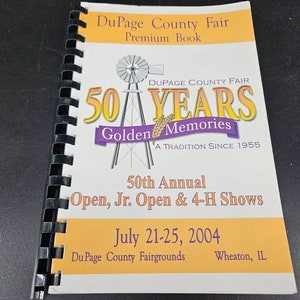 Op de afbeelding: Een geel en wit boekje met een zwarte spiraalbinding. De omslag heeft een windmolenafbeelding en de tekst "DuPage County Fair 50 Years Golden Memories A Tradition Since 1955". De tekst "50th Annual Open, Jr. Open & 4-H Shows" staat ook op de omslag, samen met de data "July 21-25, 2004" en de locatie "DuPage County Fairgrounds Wheaton, IL".