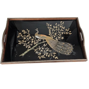 Könnte beinhalten: Ein schwarzes Serviertablett mit Holzrahmen zeigt ein goldenes und braunes Pfauenmotiv auf schwarzem Hintergrund. Der Pfau sitzt auf einem goldenen Ast mit goldenen Blättern.