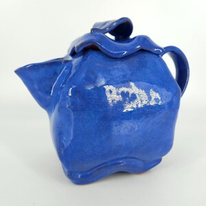 May include: A blue ceramic teapot with a unique, wavy design. The teapot has a silver inscription that reads "Robin".