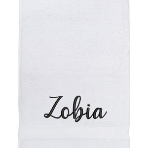 May include: White bath towel with the name "Zobia" embroidered in black cursive lettering.