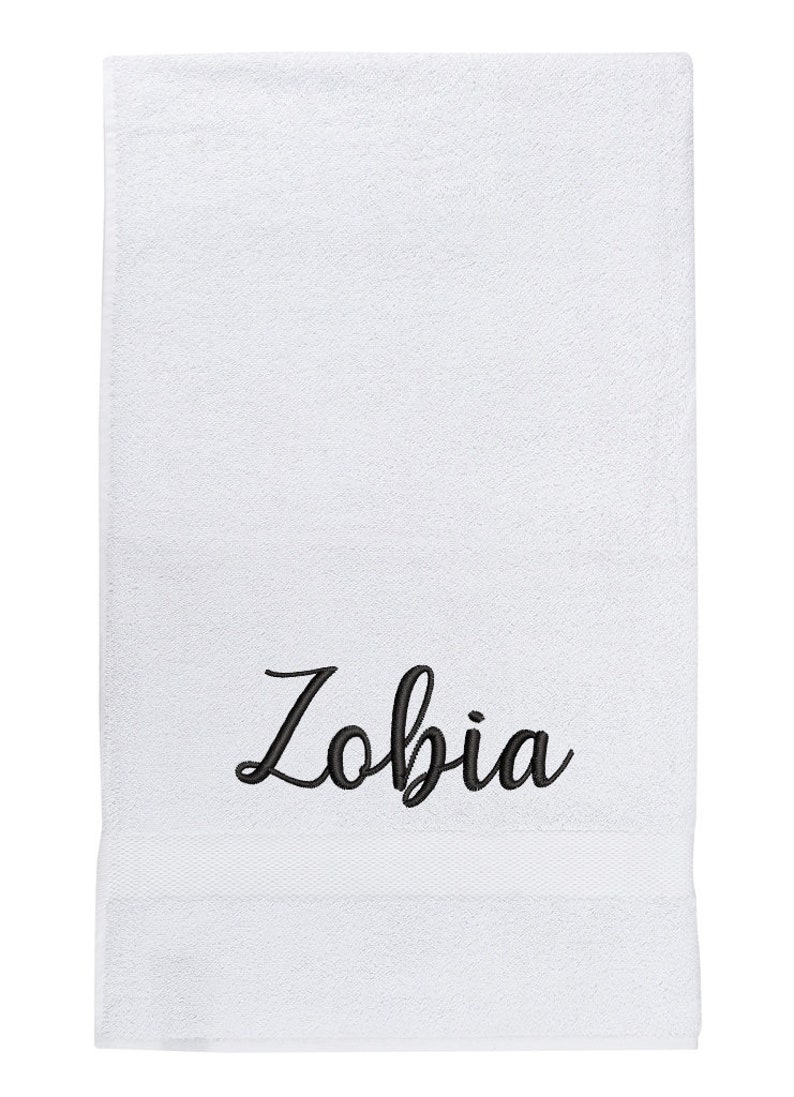 May include: White bath towel with the name "Zobia" embroidered in black cursive lettering.