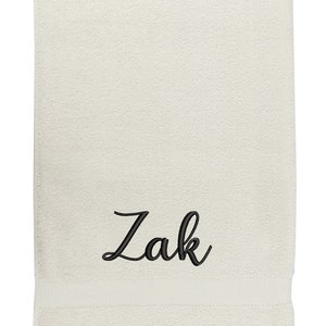May include: A white towel with the name "Zak" embroidered in black cursive lettering.