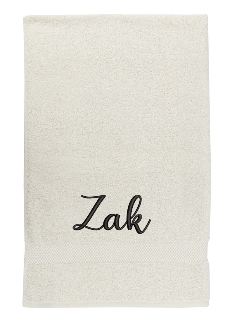 May include: A white towel with the name "Zak" embroidered in black cursive lettering.
