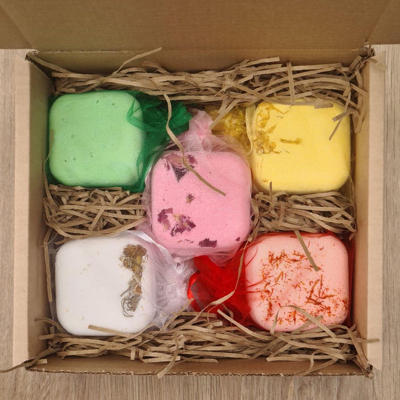 The open gift box depicting our serene selection. A floral, calming, anti-anxiety, post workout and focus booster steamer in our provided organza bags, thoughtfully arranged and surrounded with packing hay