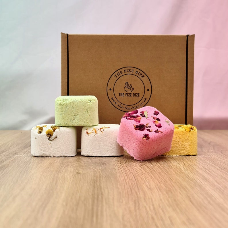 5 of our shower steamers (Calming, Anti-Anxiety, Floral, Focus Booster and Post-Workout) artfully arranged in front of their presentation box. For information on their scents refer to scent page. For information on their size use the dimension page.