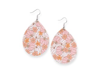 May include: A pair of teardrop-shaped earrings featuring a repeating pattern of light pink and white pumpkins interspersed with small orange flowers on a white background, suspended from silver-toned metal fishhook ear wires.