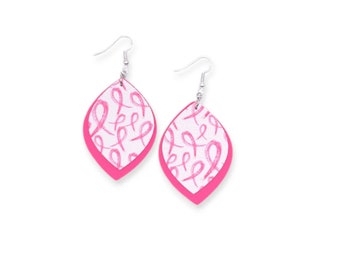 May include: A pair of teardrop-shaped earrings featuring a white surface printed with a repeating pattern of pink awareness ribbons. Each earring has a solid hot pink backing layer and is attached to a silver-toned metal fishhook ear wire.